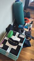 Photo showing boxed black blankets or towels with black 'Do not Disturb' eye masks on top alongside a rolled yoga mat and various health accessories on the floor.