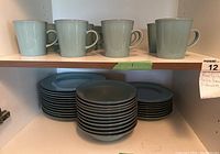 Blue-gray mugs on top shelf with matching dinner and salad plates underneath shelf.