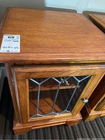 Full view of wooden side table top and leaded glass door with metal knob.