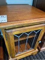 Top and front view of the wood side table showing the leaded glass door and wood grain top with scratches.