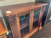 Full view of wooden sideboard with stained glass front doors and carved wood on corners