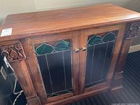 Top-front view of the wooden sideboard showing stained glass doors with green and black glass and carved wooden corner accents.