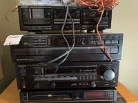 Stack of Kenwood stereo components including double cassette deck, compact disc player, and stereo receiver with visible cables on top.