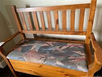 Front view of wooden storage bench with slatted backrest and multicolor fabric seat cushion.