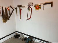 Wide view of the basement corner showing various tools hung on the wall including saws, axes, and power tools on the floor.