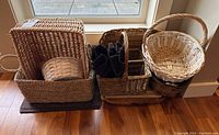 Overview of multiple wicker baskets, cutting boards and placemats on hardwood floor near window