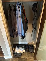 Photo of six women’s jackets hanging on a rod in a closet. Below the jackets are four pairs of shoes and a black purse on the floor.
