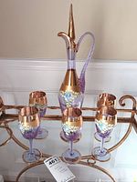Photo showing full set of one decanter with tall stopper and six wine glasses arranged on a glass-top table.