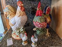 Front view of two large colorful ceramic roosters and a pair of Fitz & Floyd hen salt and pepper shakers on a granite countertop.