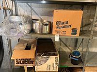 Shelving unit with cookware including clam steamer pots in box, stock pot with lid, electric deli slicer box, roasting pan, and other kitchen items