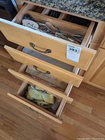 Three drawers in a wooden kitchen cabinet showing folded kitchen linens in bottom drawers and partially visible flatware in top drawer.