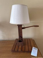 Full view of wooden fountain-style table lamp with cream shade on wooden table.