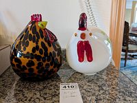 Frontal view of two hand blown glass chickens on a granite surface with price tag in front.