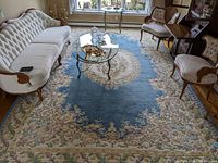 Blue floral Kalahbar Persian rug shown in living room setting with couches and glass coffee table, visible full length and detail of pattern.