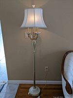 Full view of the Lenox floor lamp showing the brass and white ceramic base, three candle-style bulbs, and white fabric lampshade with braided trim paired with a decorative finial.