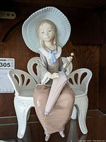 Front view of the Lladro figurine showing the seated young woman holding an umbrella on a white bench.