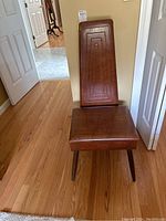 Front view of brown vinyl padded chair showing geometric stitched pattern on backrest and seat with tapered wooden legs.