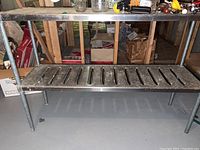 Full view of metal shelf showing top horizontal surface with small items on it, vented lower shelf, and tubular leg supports