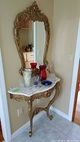 Full view of mirror and marble top table showing their placement against wall with glassware on table.