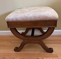 Side view of the ottoman showing wooden curved X-base and patterned upholstered cushioned seat.