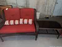 Loveseat and coffee table in brown resin wicker with red cushions and striped pillows shown against concrete wall