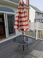 Patio table and closed umbrella on a wooden deck near white railing and sliding glass door