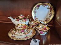 Frontal view of entire tea set including teapot, cups, saucer, plates, creamer, and sugar bowl on wooden shelf