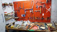 Wide view of workbench with assorted hand tools and hardware organized on pegboard and table