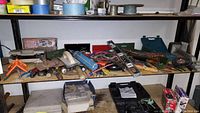 Shelf view of assorted hand tools including hammers, pliers, clamps, and other tools organized loosely on shelves.