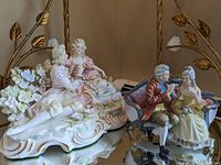 First figurine: Victorian couple reclining on floral loveseat, detailed attire, with integrated lamp and music box base