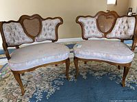Front view of both Victorian styled chairs showing their tufted upholstered cushions, floral fabric, cane backs with carved wood frames, and curved legs.