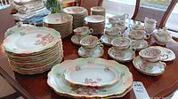 Large assortment of plates, teacups, saucers, and serving dishes arranged on a dining table showing the floral pattern and gilded edges.