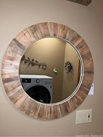 Full view of the round wall mirror mounted on a beige wall, showing the wooden slat frame and reflective mirror surface.
