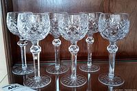 Front view of six crystal wine glasses arranged in two rows on glass shelf