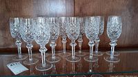 Front view of twelve crystal champagne flutes arranged in two rows on wooden shelf