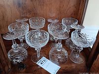 Front view of 12 crystal coupe glasses on wood shelf