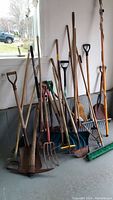 Wide angle photo showing a collection of garden and snow tools leaning against a wall