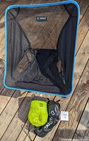 Top-down view of Helinox camp chair frame and mesh seat with two packed items below, tarp and carrying bag.