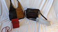 Four purses displayed on a white sheet: large tan and black leather tote, brown leather crossbody purse, small red purse, silver clutch in pouch.