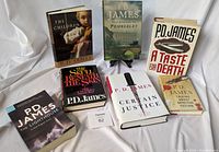Photo showing six hardcover books and one paperback book by P.D. James arranged on white cloth. Titles visible include 'The Children of Men', 'Death Comes to Pemberley', 'A Taste for Death', 'The Private Patient', 'Certain Justice', 'Adam Dalgliesh Detective Fiction', and the paperback 'The Lighthouse'.
