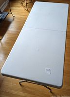 Folded white plastic folding table laid out flat on wood floor, showing full tabletop surface.