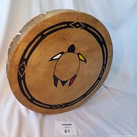 Handcrafted traditional hand drum showing front design of a turtle with tribal pattern and painted colors on rawhide drumhead.