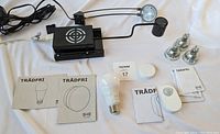 IKEA Tradfri smart lighting devices including smart bulb, motion sensor, remote control, circular dimmer, and manuals, along with two black IKEA cabinet lights from Grundtal and Gruva series with cords and mounting hardware.