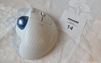 Logitech Ergo M575 wireless trackball mouse close-up showing white body, blue trackball, and buttons.