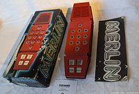 Photo showing the Merlin game, its original box with visible wear, and the instruction manual laid out on a table.