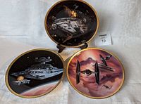 Set of three Star Wars collector plates displayed on a white cloth background showing Millennium Falcon, Star Destroyer, and TIE Fighters designs.