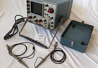 Full view of Tektronix oscilloscope, included probes, and removable protective cover placed on white fabric background.