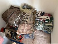 Overall view of stacked braided rugs and hooked rugs showing various color patterns and condition.
