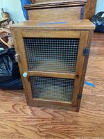 Front view of small wood cabinet featuring wire mesh door and turning latch on left side.