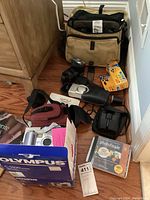 Tan padded camera bag, Canon flash, Olympus C-5500 box, silver digital camera, Kodak film, binoculars, Photofinale CD laid out on floor